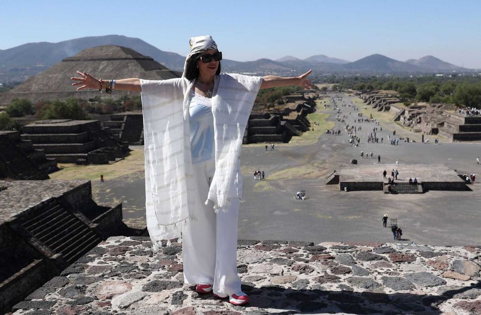 Woman in white standing at Teotihuacan pyramids with arms outstretched.