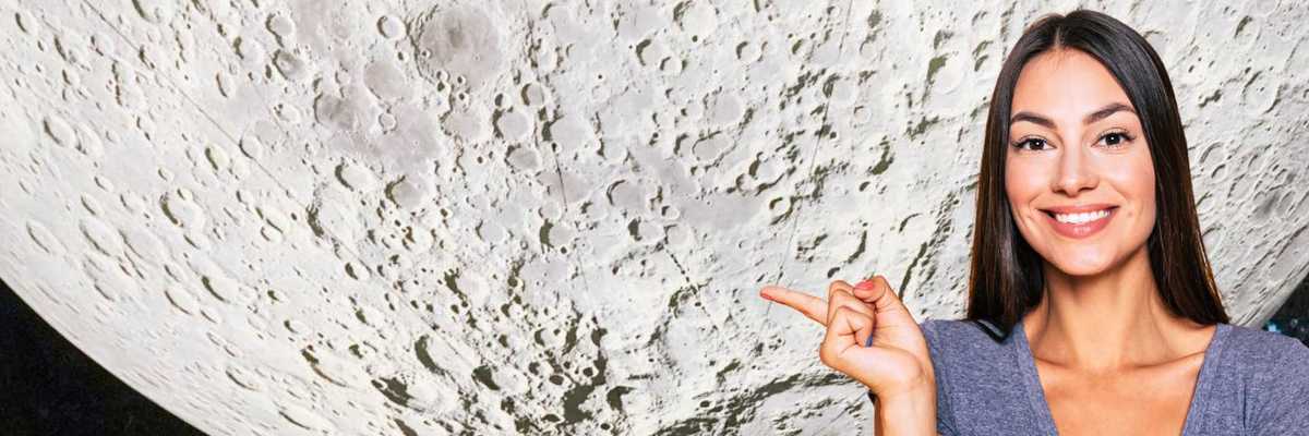 Woman smiling and pointing at a large moon surface backdrop.
