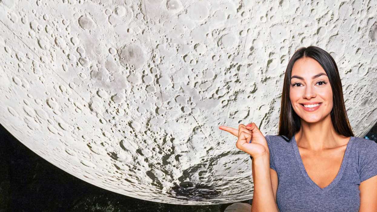 Woman smiling and pointing at a large moon surface backdrop.