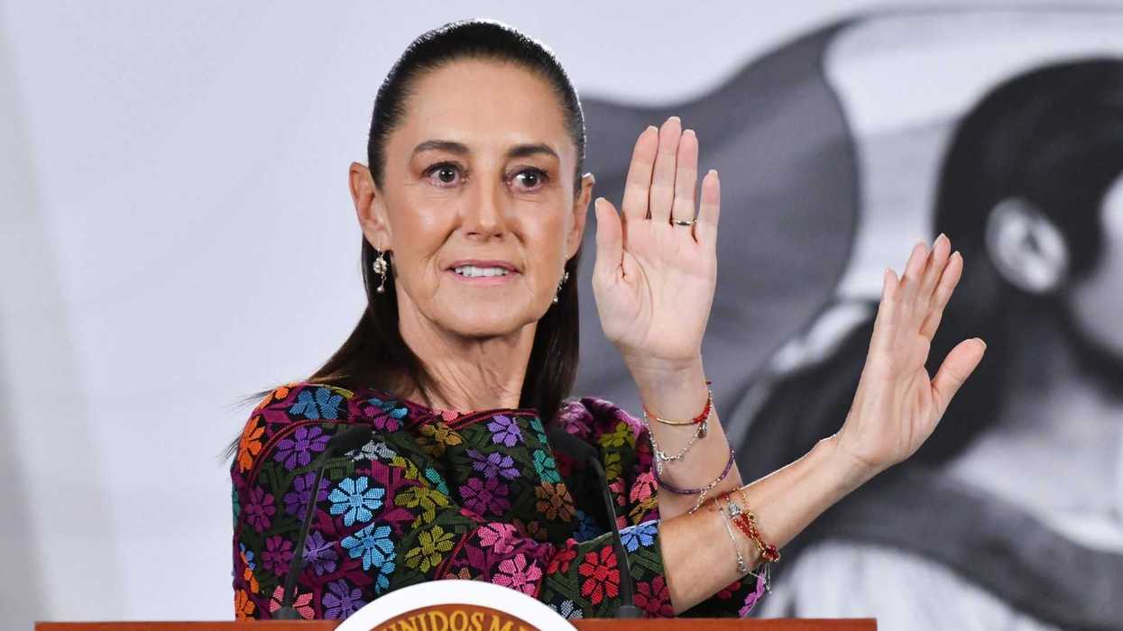 Woman speaking at a podium, gesturing with hands raised.