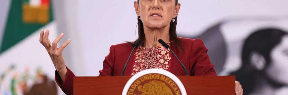 Woman speaking at a podium with a Mexican emblem, flag in background.
