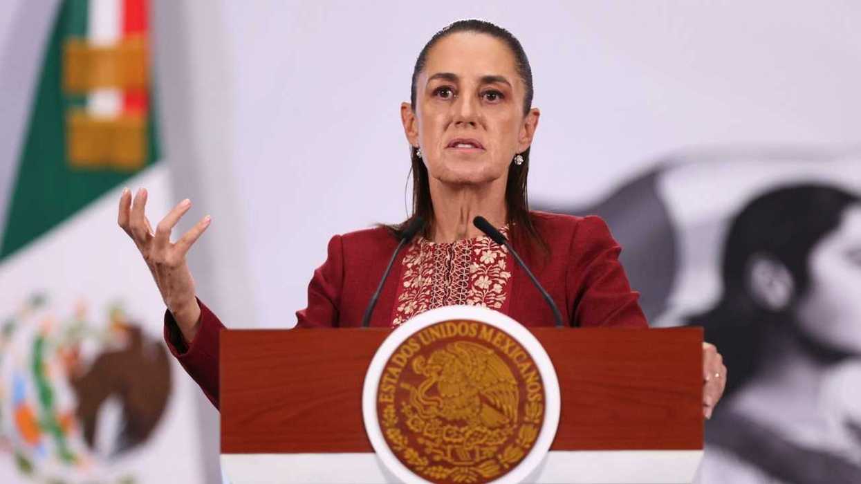 Woman speaking at a podium with a Mexican emblem, flag in background.