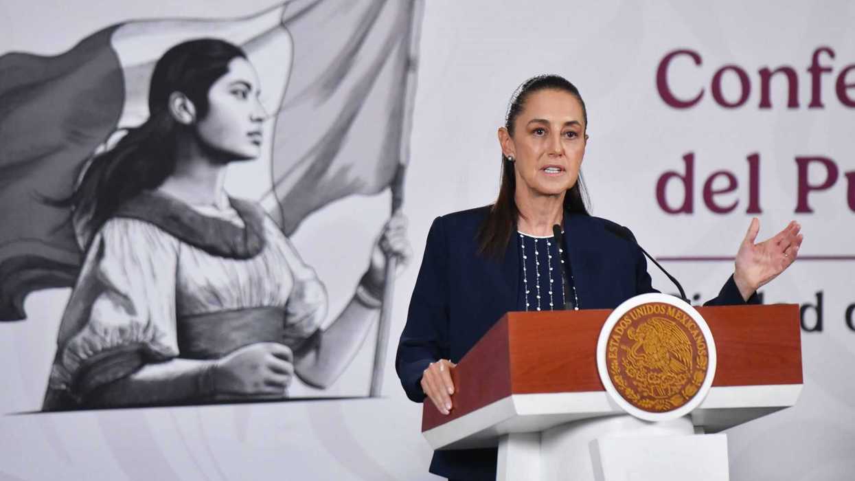 Woman speaking at a podium with a mural of a woman holding a flag behind her.