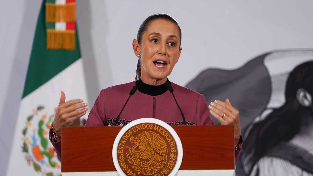 Woman speaking at a podium with Mexican emblem, flag in background.