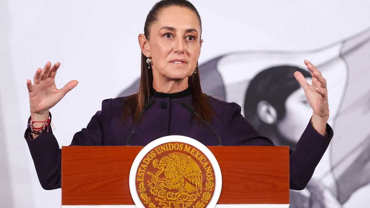 Woman speaking at a podium with the Mexican emblem, gesturing with both hands.