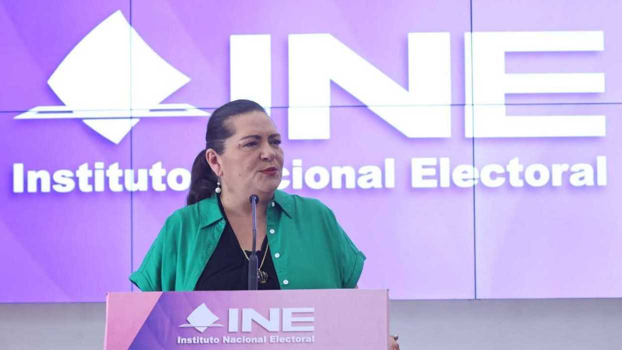 Woman speaking at an INE podium with a purple backdrop.