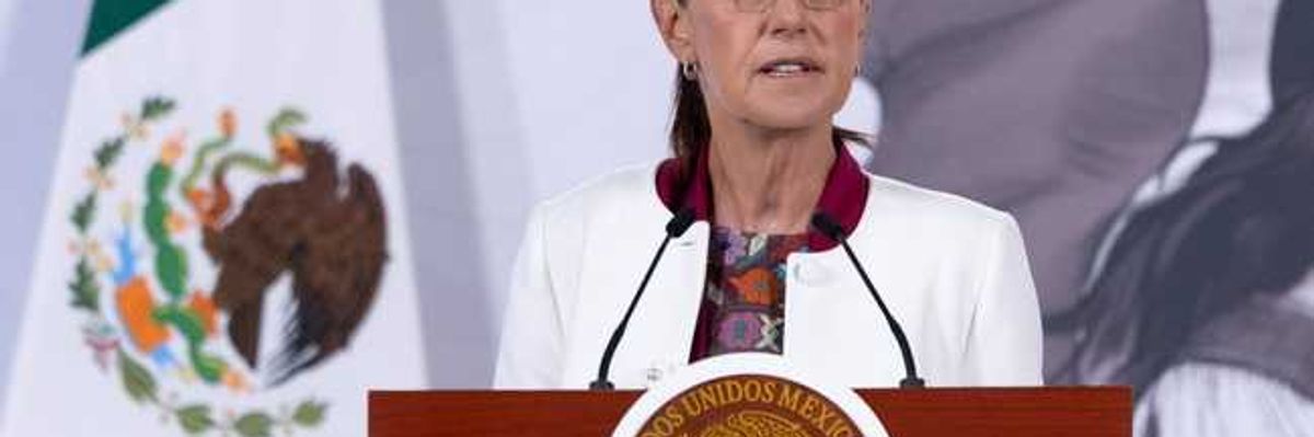Woman speaking at podium with Mexican seal and flag in the background.