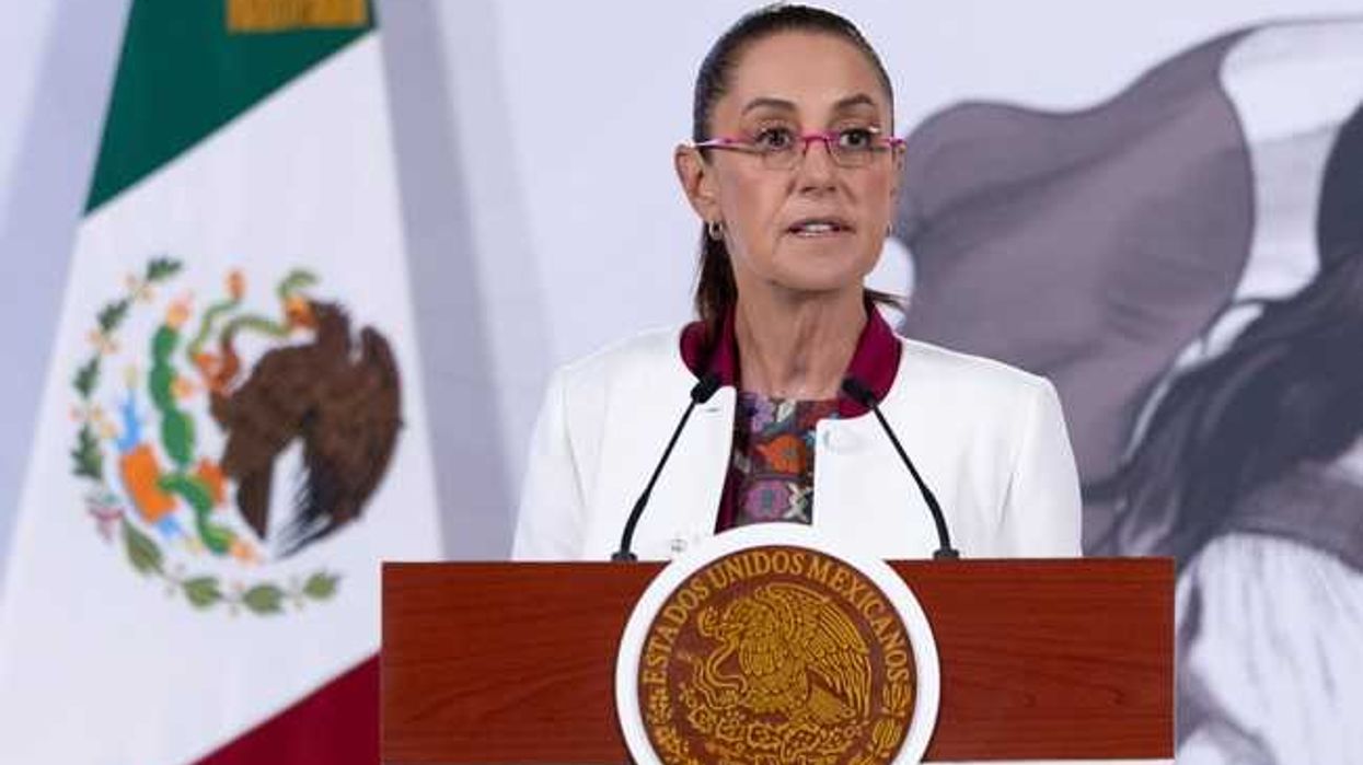 Woman speaking at podium with Mexican seal and flag in the background.
