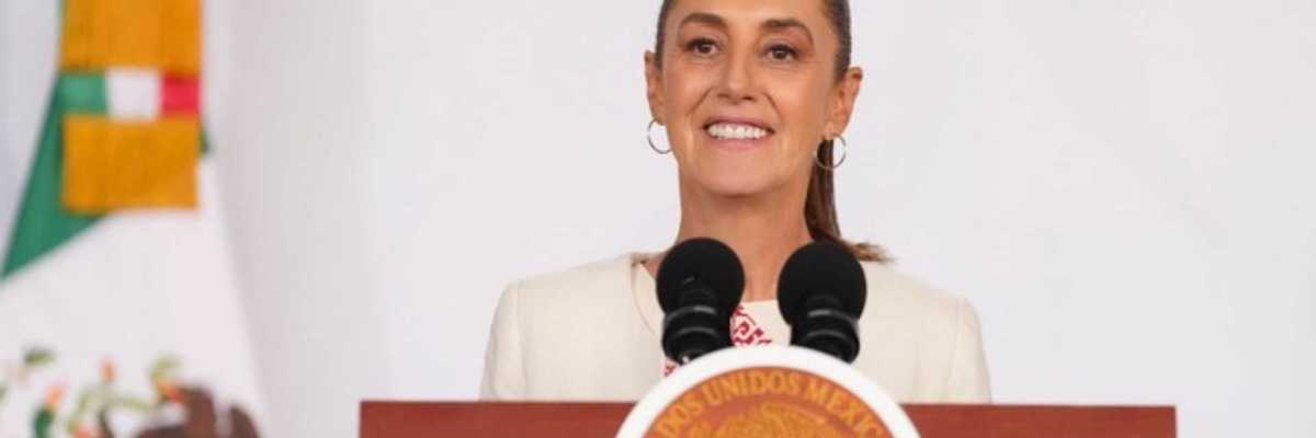 Woman speaking live at a podium with Mexican flag emblem.