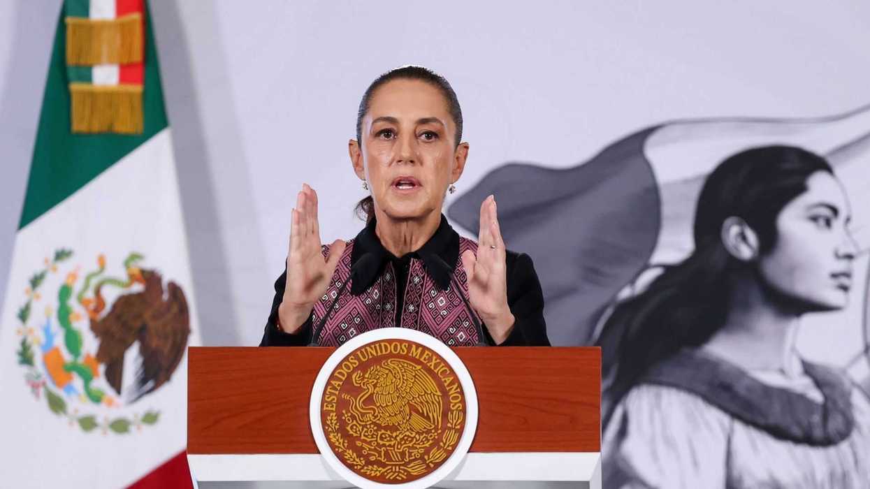 Woman speaks at a podium with a Mexican flag background.