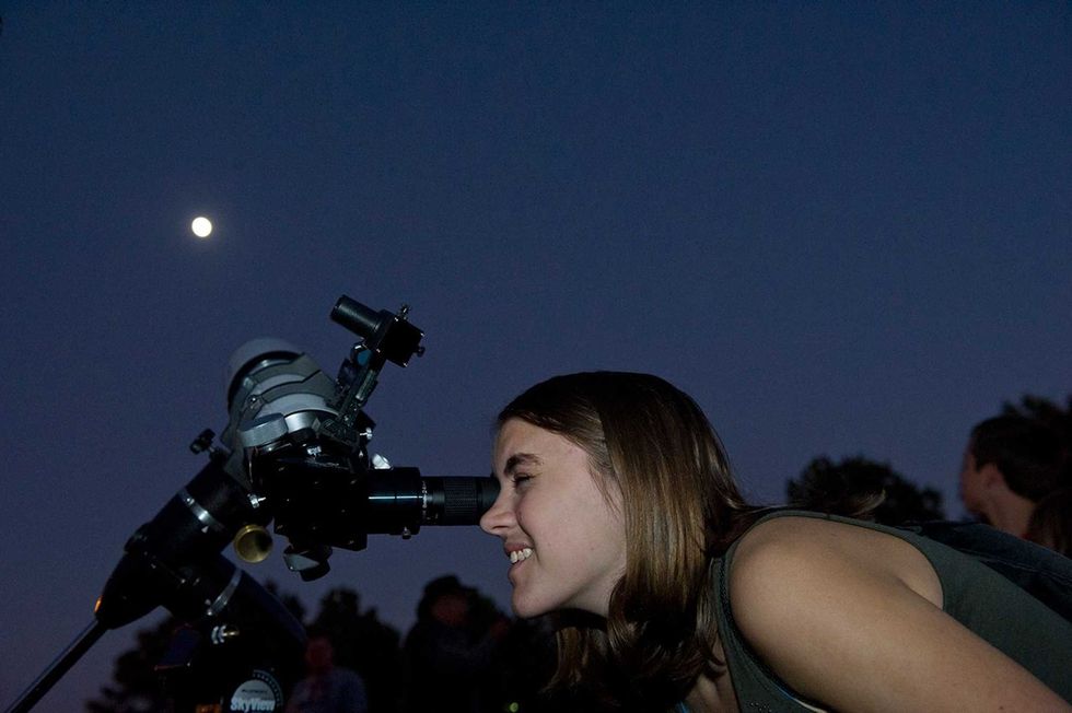 Woman using a telescope at night, moon visible in the sky.