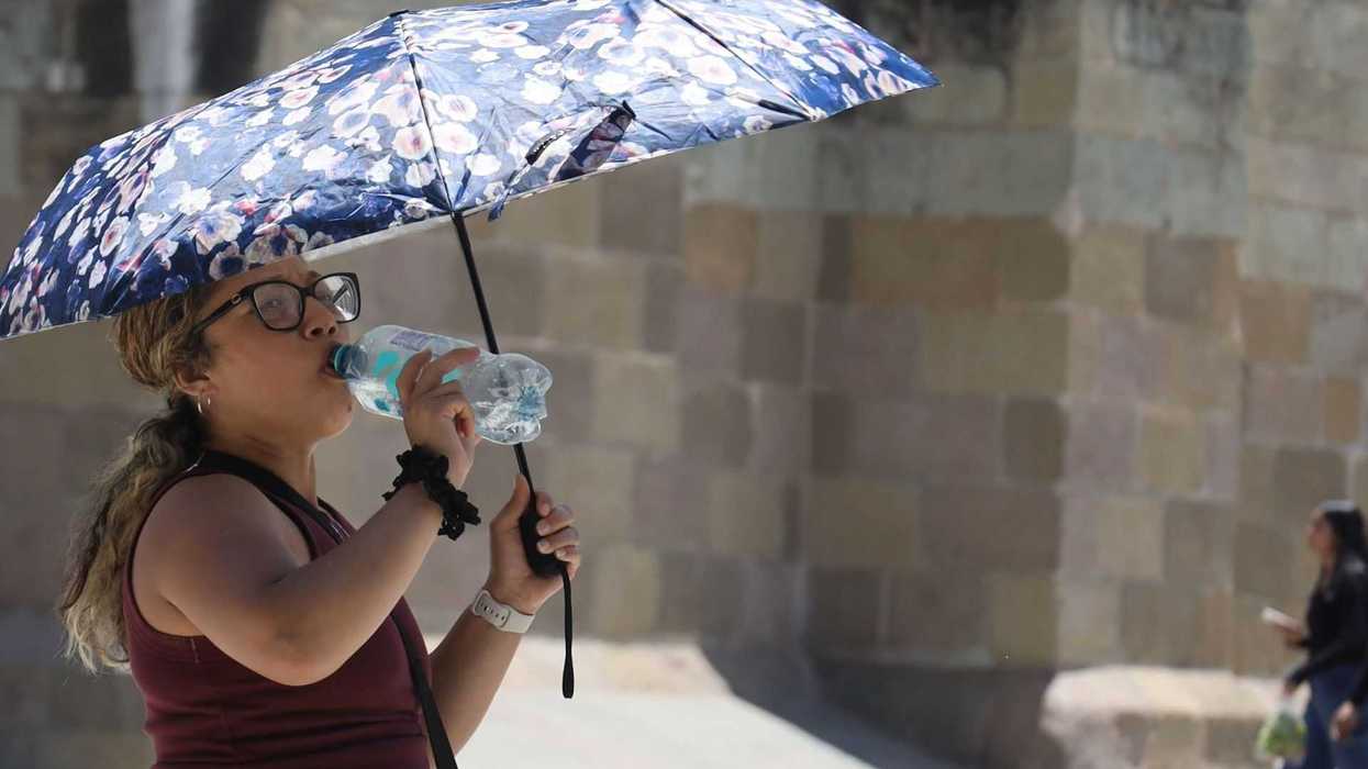 Woman with a floral umbrella drinks water on a sunny day.