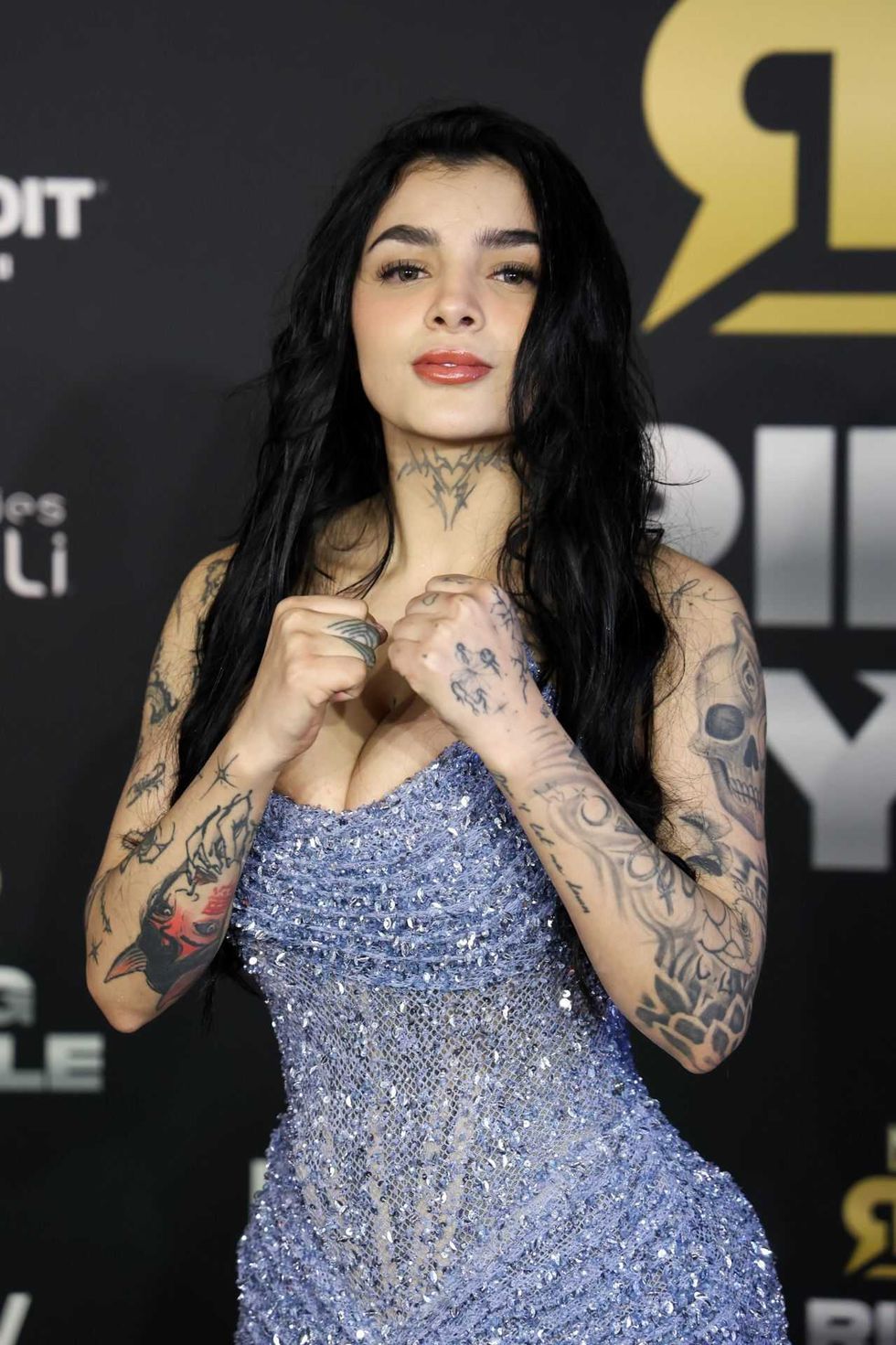Woman with tattoos in sparkly dress poses on red carpet.