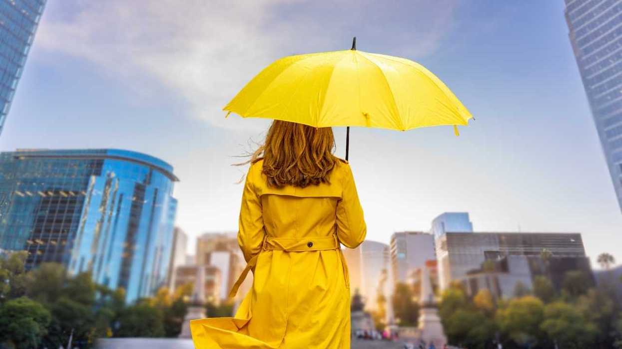 Woman with yellow umbrella and coat in cityscape.