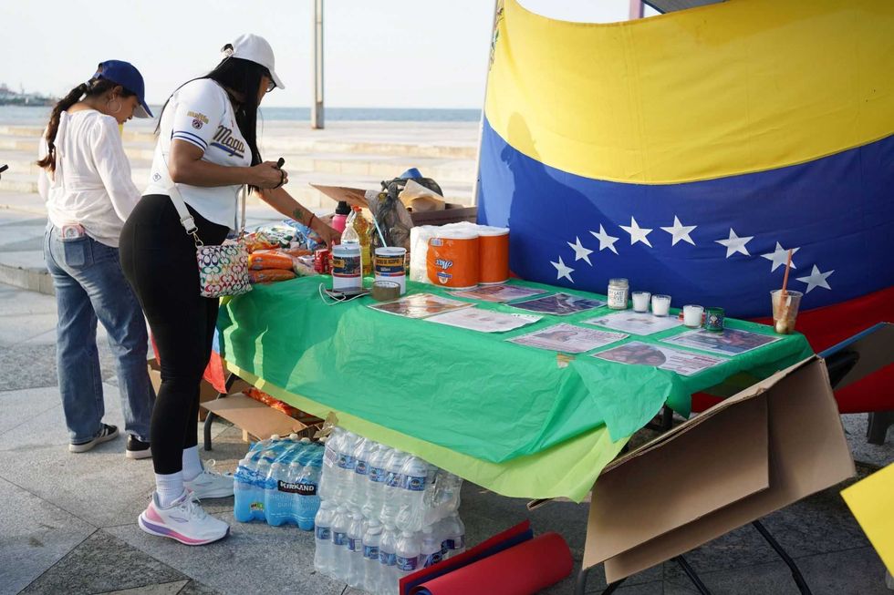 Women arranging items on a table with a Venezuelan flag backdrop.