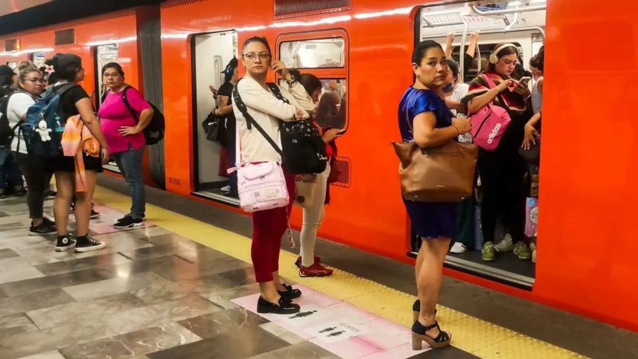 Women waiting at a crowded metro station with an orange train and open doors.
