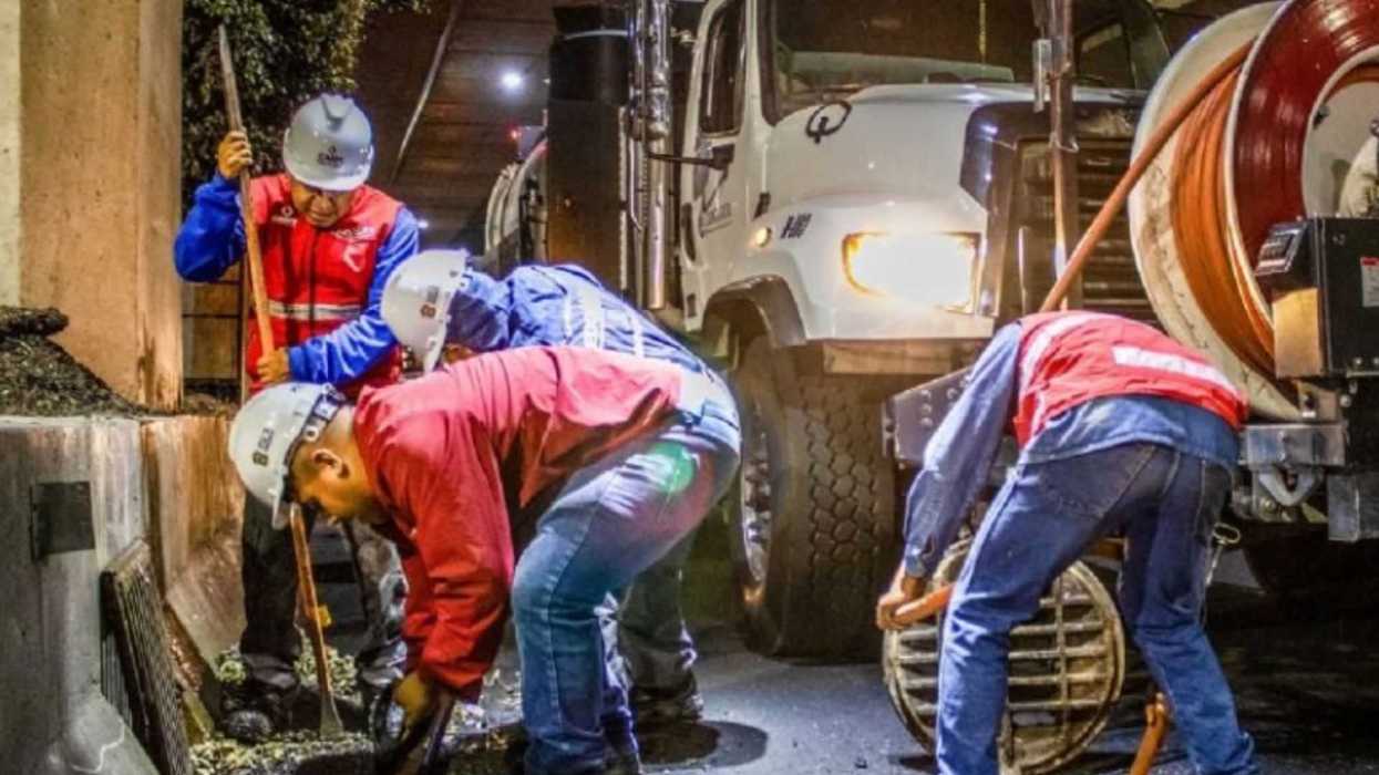 Workers in hard hats clean a drain beside a truck during nighttime road maintenance.