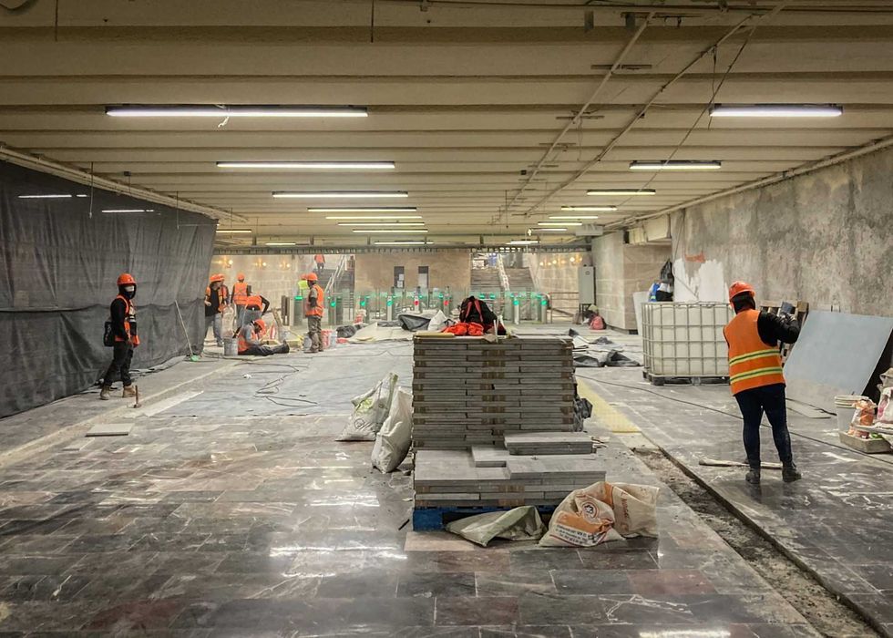 Workers in safety gear renovating a spacious underground metro station.