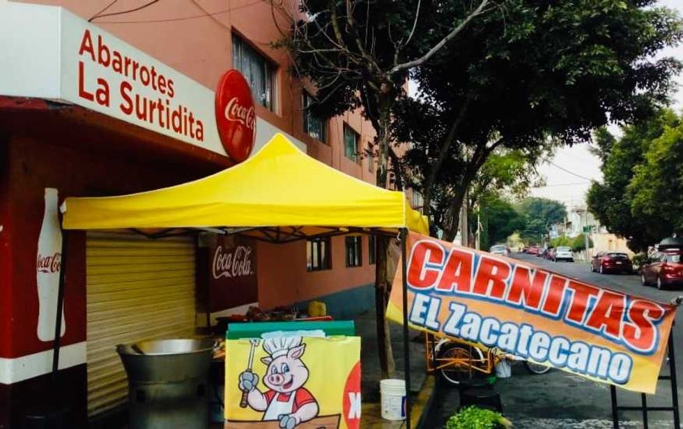 Yellow tent with "Carnitas El Zacatecano" sign next to a store on a quiet street.
