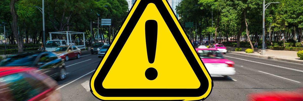 Yellow warning sign with exclamation mark on busy city street.