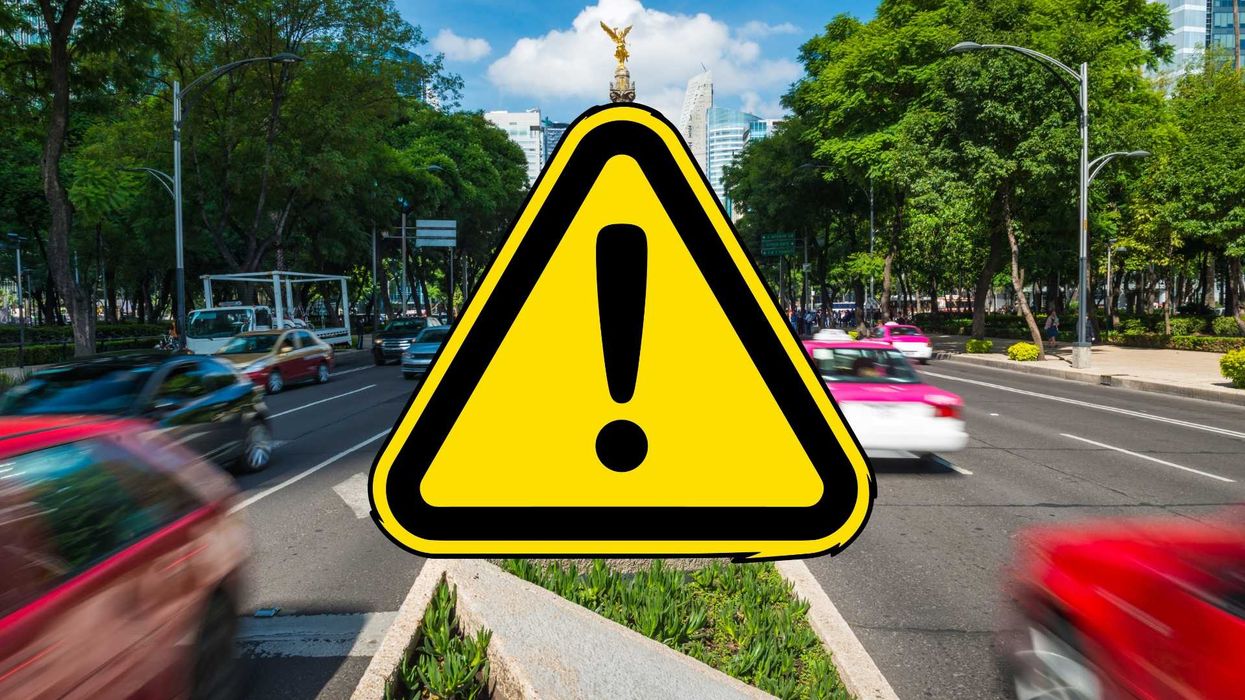 Yellow warning sign with exclamation mark on busy city street.